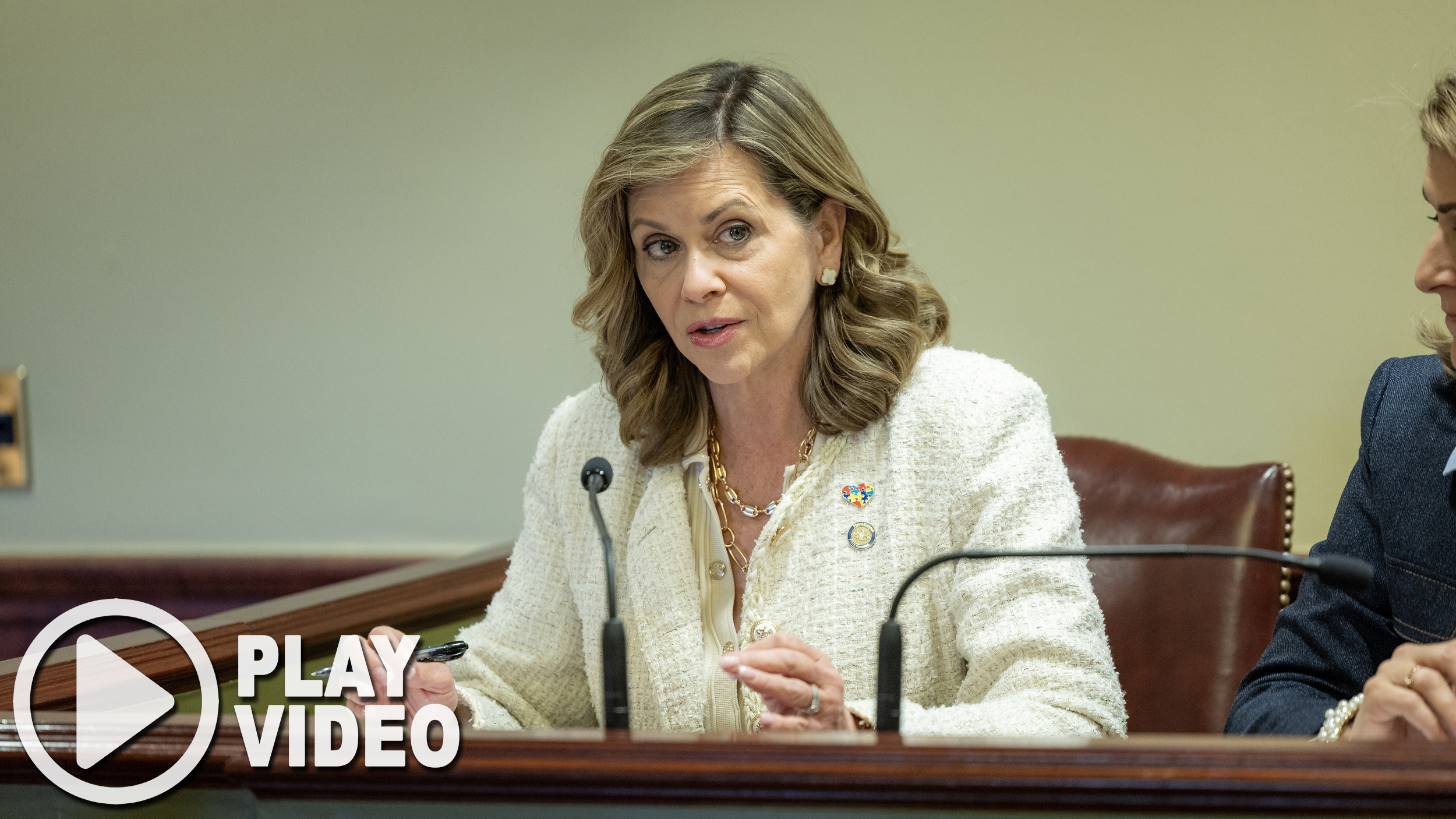 Sen. Camera Bartolotta speaking into microphone with caption “play video”