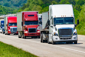 A solid line of eighteen-wheelers barrel down an interstate highway in Tennessee. Heat waves rising from the pavement give a nice shimmering effect to vehicles and trees behind the lead truck.