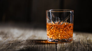 A glass of whiskey is sitting on a wooden table top.