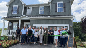 Sen. Bartolotta stands with a large group of people in front of a model home about to cut a ceremonial ribbon.