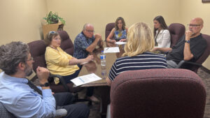 Sen. Bartolotta sits at the head of a conference table with many people sitting with her in mid discussion.